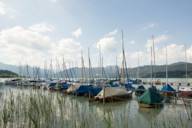 Boote liegen am Steg auf dem Tegernsee bei München. Im Hintergrund sind die Münchner Hausberge zu sehen.